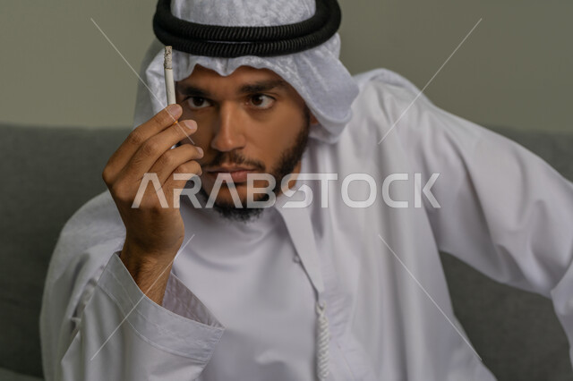 ايماءات تدل على الحذر من ادمان السجائر، التوقف عن اتباع العادات السلوكية الضارة، صورة مقربة لشاب عربي خليجي إماراتي يقوم بالنظر إلى لفافة التبغ بتعابير الرفض وعدم الرضا، محاربة عادة التدخين، المعاناة من الاضطرابات النفسية والمشاكل الصحية