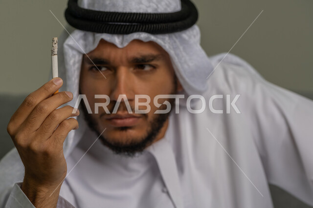 محاربة عادة التدخين، ايماءات تدل على الحذر من ادمان السجائر، التوقف عن اتباع العادات السلوكية الضارة، صورة مقربة لشاب عربي خليجي إماراتي يقوم بالنظر إلى لفافة التبغ بتعابير الرفض وعدم الرضا، المعاناة من الاضطرابات النفسية والمشاكل الصحية