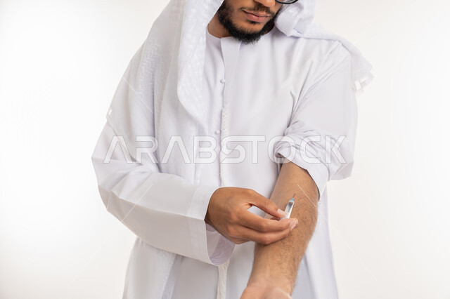 المعاناة من الاضطرابات النفسية والمشاكل الصحية، تعاطي المخدرات عن طريق الحقن في الأوردة، القيام بعادات سلوكية ضارة وتعاطي المواد السامة، بورتريه مقرب لأيدي شاب عربي خليجي إماراتي يرتدي الكندورة يقوم بأخذ ابرة مخدرة، خلفيه بيضاء