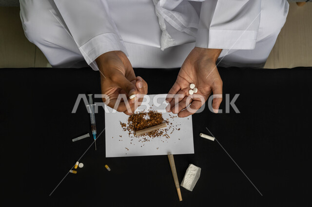 تعاطي المواد السامة، القيام بعادات سلوكية ضارة، المعاناة من الاضطرابات النفسية والمشاكل الصحية، صورة مقربة لأيدي رجل عربي خليجي إماراتي يمسك  مجموعة من الحبوب مخدرة، الآثار السلبية للادمان والتعاطي