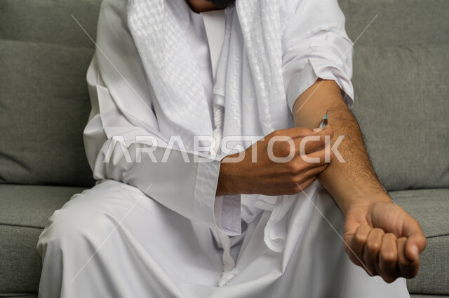 المعاناة من الاضطرابات النفسية والمشاكل الصحية، تعاطي المخدرات عن طريق الحقن في الأوردة، الآثار السلبية للادمان، القيام بعادات سلوكية ضارة وتعاطي المواد السامة، صورة مقربة لرجل عربي خليجي إماراتي يرتدي الكندورة والغترة البيضاء يقوم بأخذ جرعة مخدرة