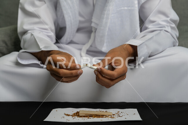 التوقف عن اتباع العادات السلوكية الضارة وتعاطي المواد السامة، صورة مقربة لأيدي شاب عربي خليجي إماراتي يقوم بإتلاف لفافة تبغ، محاربة عادة التدخين، ايماءات تدل على الحذر من ادمان السجائر