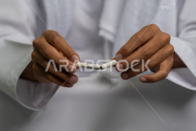 التوقف عن اتباع العادات السلوكية الضارة وتعاطي المواد السامة، صورة مقربة لأيدي شاب عربي خليجي إماراتي يقوم بإتلاف لفافة تبغ، محاربة عادة التدخين، ايماءات تدل على الحذر من ادمان السجائر