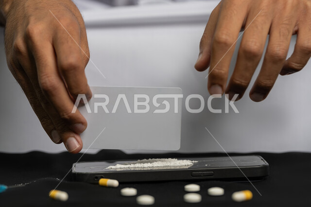 الآثار السلبية للادمان، القيام بعادات سلوكية ضارة، تعاطي المواد السامة، المعاناة من الاضطرابات النفسية والمشاكل الصحية، صورة مقربة لأيدي شاب عربي خليجي إماراتي يرتدي الكندورة والغترة يقوم بتحضير البودرة البيضاء لاستنشاقها