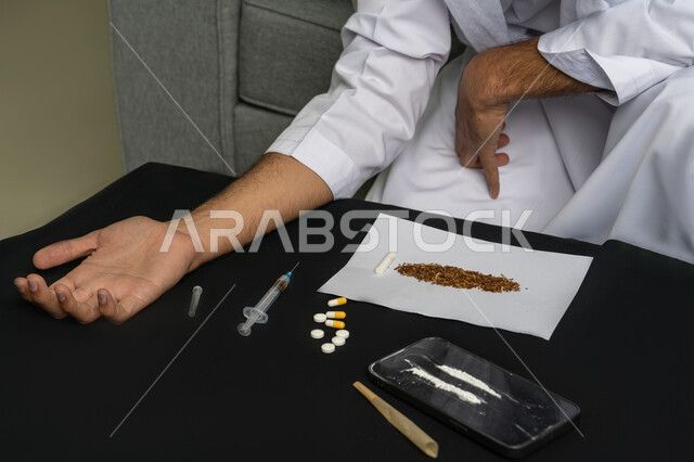 Intravenous drug use, suffering from mental disorders and health problems, engaging in harmful behavioral habits and taking toxic substances, close-up of the hand of a young Arab Gulf Emirati man wearing a kandura taking a narcotic injection