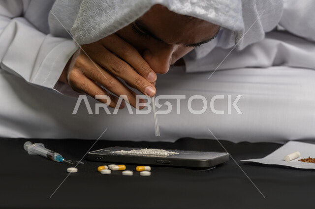 القيام بعادات سلوكية ضارة، تعاطي المواد السامة عن طريق استنشاقها، المعاناة من الاضطرابات النفسية والمشاكل الصحية، الآثار السلبية للادمان، صورة مقربة لرجل عربي خليجي إماراتي يرتدي الكندورة والغترة يقوم باستنشاق المخدرات