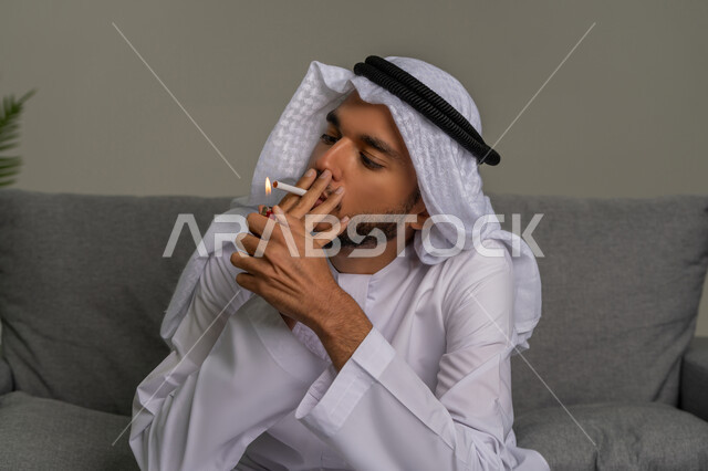 إيماءات الشعور بالنشوة عند دخول النيكوتين للجسم، الإصابه بأمراض الجهاز التنفسي، صورة مقربة لشاب عربي خليجي إماراتي يرتدي الكندورة والغترة البيضاء يقوم بإشعال سيجارة، الادمان على التبغ والسجائر، تعاطي مواد ضارة وسامة، عادات سلوكية خاطئة