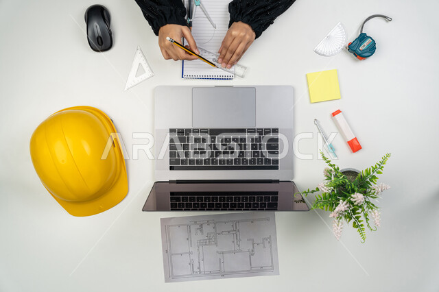 عرض ومراجعة مخطوطات المشاريع, العمل في القطاع الهندسي, دراسة أساسيات المحطط الإنشائي, بورتريه علوي عامودي ليدي مهندسة عربية خليجية اماراتية تعمل على الحاسوب المحمول، امرأة سعودية امام مكتب عليه خوذة الحماية والمخططات، إدارة ومتابعة المشروع, خلفية بيضاء