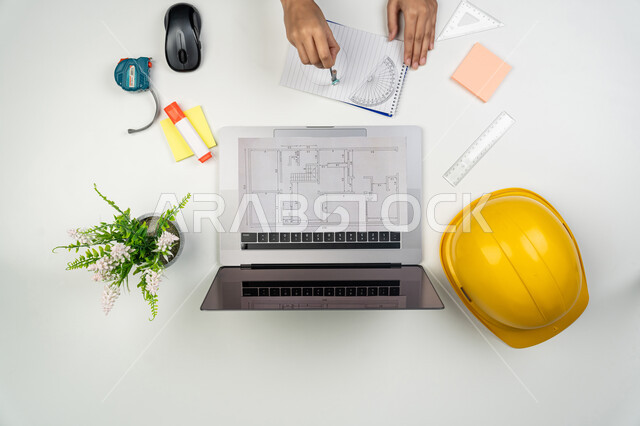 دراسة أساسيات المحطط الإنشائي, العمل في القطاع الهندسي, بورتريه علوي عامودي ليدي مهندسة عربية خليجية اماراتية تعمل على الحاسوب المحمول، امرأة سعودية امام مكتب عليه خوذة الحماية والمخططات، مراجعة وعرض مخطوطات المشاريع, إدارة ومتابعة المشروع, خلفية بيضاء