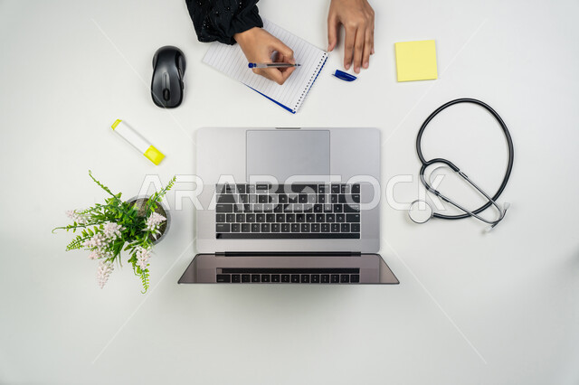 اعطاء الاستشارات للمرضى عن بعد عبر الحاسوب، مفهوم الرعاية الصحية، دمج التقنيات الحديثة بالمجالات الطبية, تطور القطاع الصحي، بورتريه علوي عامودي ليدي طبيبة عربية خليجية اماراتية تستخدم اللابتوب بجانبها سماعات طبية، سيدة سعودية تعمل في مجال الطب، خلفية بيضاء