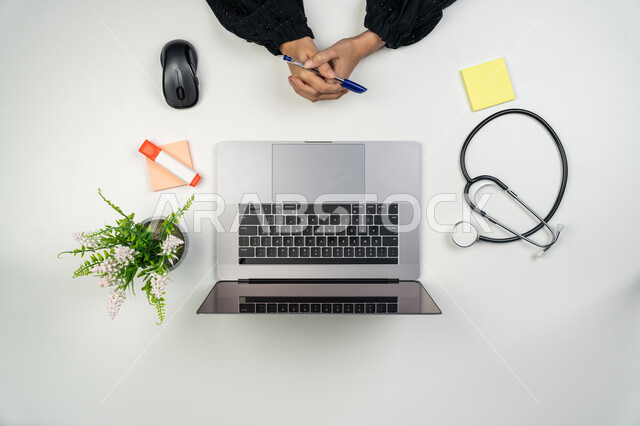 دمج التقنيات الحديثة بالمجالات الطبية, تطور القطاع الصحي، تقديم الاستشارات للمرضى عن بعد عبر الحاسوب، بورتريه علوي عامودي ليدي طبيبة عربية خليجية اماراتية تستخدم اللابتوب بجانبها سماعات طبية، سيدة سعودية تعمل في مجال الطب، مفهوم الرعاية الصحية، خلفية بيضاء