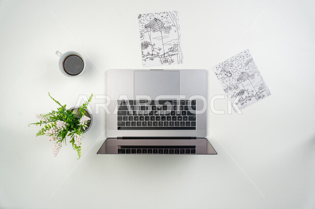 الشراء والبيع عبر الانترنت، التدريب والتعلم من خلال المواقع الإلكترونية، صورة علوية عامودية لجهاز الحاسوب المحمول مع أوراق مرسوم عليها وكوب من القهوة، الحصول على الألوان المائية والخشبية ومستلزمات الرسم أونلاين، خلفية بيضاء