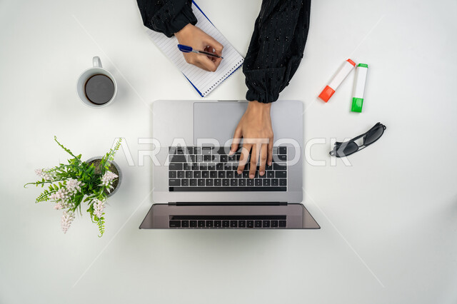 انجاز مهام العمل عن بعد، تدوين الملاحظات والأفكار، بورتريه علوي عامودي ليدي امرأة عربية خليجية اماراتية تقوم بالكتابة على دفتر وبجانبها وأقلام ملونة ونظارات شمسية، سيدة سعودية تستخدم جهاز الحاسوب، استخدام الأجهزة التقنية الحديثة في الأعمال، خلفية بيضاء