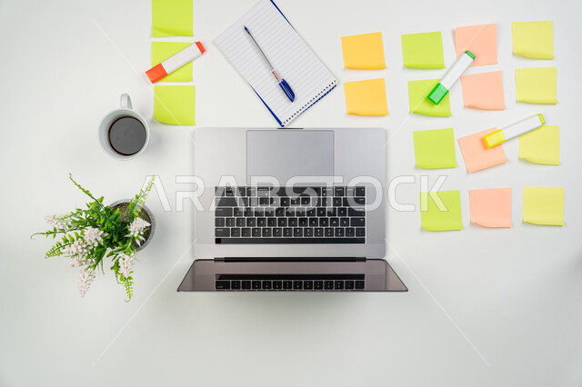 Writing down ideas and taking notes, pinning colorful memorabilia, using modern and advanced technical devices in household chores, completing work tasks remotely, vertical overhead view of laptop and a set of stationery on an office table, white background