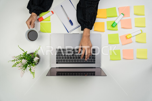 Taking notes and jotting down ideas, using modern technology devices in household chores, pinning colorful memorabilia notes, vertical overhead portrait of a Gulf Arab Emirati woman working on a laptop, young Saudi woman doing work tasks remotely, white background