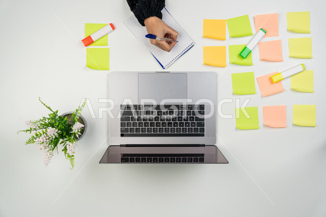 استعمال الأجهزة التقنية الحديثة في الأعمال المنزلية، تثبيت أوراق ملاحظات تذكارية ملونة، تسجيل الملاحظات ووتدوين الأفكار، بورتريه علوي عامودي لايدي امرأة عربية خليجية اماراتية تعمل على الحاسوب المحمول، شابة سعودية تقوم بانجاز مهام العمل عن بعد، خلفية بيضاء