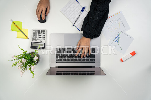 ارتفاع وإنخفاض نسبة الأسهم، حساب نسبة الأرباح المالية، بورتريه علوي عامودي لأيدي امرأة عربية خليجية اماراتية تعمل على جهاز الحاسوب المحمول، شابة سعودية تدون الملاحظات وتستخدم الألة الحاسبة، مهن ووظائف نسائية، متابعة مخطط الرسم البياني للنمو الاقتصادي، خلفية بيضاء