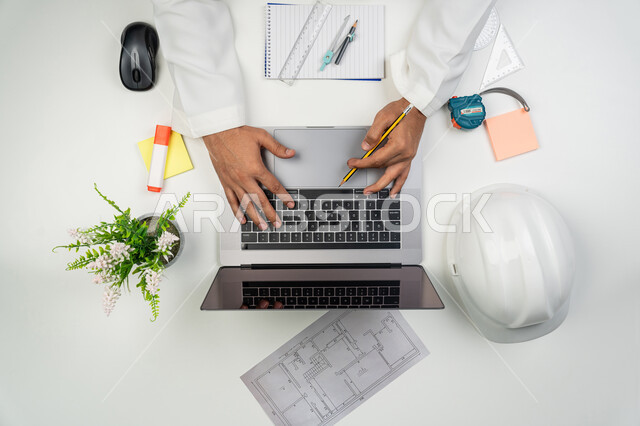 Using engineering equipment, working in the engineering sector, using advanced technologies, a vertical overhead portrait of an Arab Gulf Emirati engineer typing on a computer, using technology in practical life, white background
