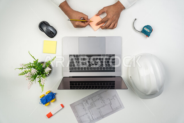 تدوين الملاحظات عن المشاريع, العمل في القطاع الهندسي, دمج التكنولوجيا الحديثة بالعمل, بورتريه علوي عامودي ليدين مهندس عربي خليجي إماراتي يقوم بالكتابة على الأوراق الملونة, استخدام التكنولوجيا في الحياة العملية, خلفية بيضاء