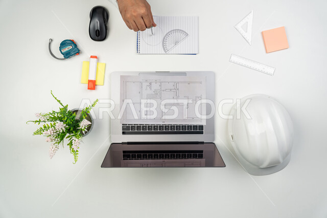 Working in the engineering sector, using engineering tools and equipment, integrating modern technology into work, a vertical overhead portrait of an Arab Gulf Emirati engineer drawing engineering plans, using technology in practical life, white background