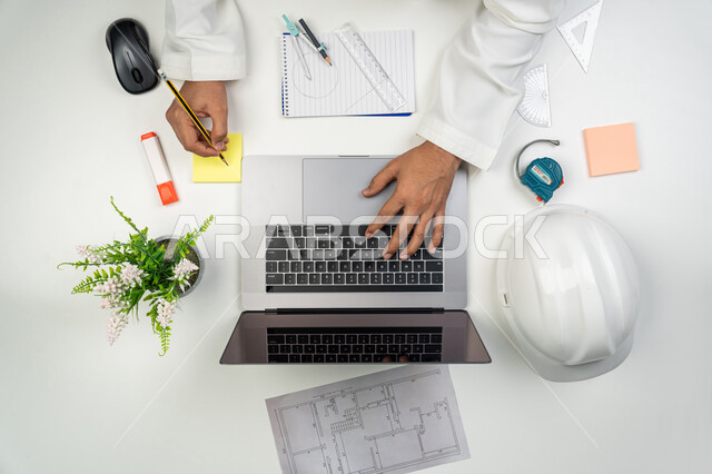 Taking important notes, integrating modern technologies into engineering work, working in the engineering sector, a vertical overhead portrait of an Arab Gulf Emirati engineer writing on colored papers, using technology in practical life, white background