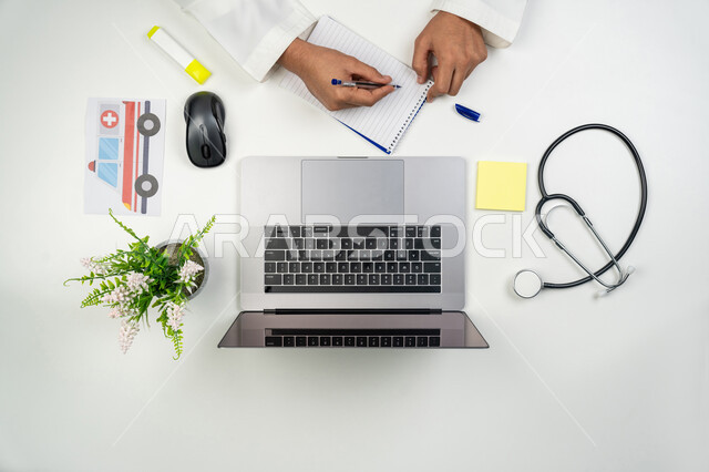 مفهوم الرعاية الصحية, تقديم الخدمات و الاستشارات عن بعد, العمل في القطاع الطبي, بورتريه علوي عامودي ليدين طبيب عربي خليجي إماراتي يقوم بكتابة وصفة طبية, استخدام جهاز الحاسوب في الحياة العملية, خلفية بيضاء