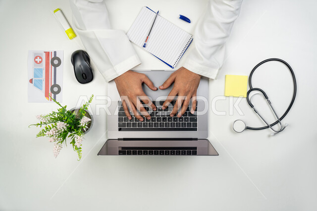 دمج التقنيات الحديثة بالأعمال الطبية, تقديم خدمات الرعاية الصحية عن بعد, العمل في القطاع الطبي, بورتريه علوي عامودي ليدين طبيب عربي خليجي إماراتي يقوم بإدخال بيانات المرضى على جهاز الحاسوب, خلفية بيضاء