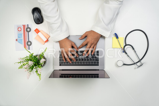 العمل في القطاع الطبي, دمج التقنيات الحديثة بالأعمال الطبية, تقديم خدمات الرعاية الصحية عن بعد, بورتريه علوي عامودي ليدين طبيب عربي خليجي إماراتي يقوم بإدخال بيانات المرضى على جهاز الحاسوب, خلفية بيضاء