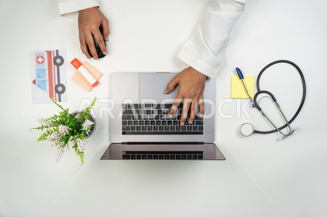 تقديم خدمات الرعاية الصحية عن بعد, العمل في القطاع الطبي, دمج التقنيات الحديثة بالأعمال الطبية, بورتريه علوي عامودي ليدين طبيب عربي خليجي إماراتي يقوم بإدخال بيانات المرضى على جهاز الحاسوب, خلفية بيضاء