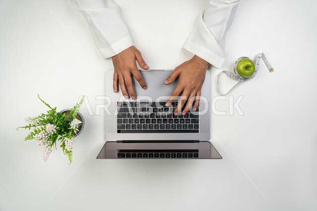 دمج التقنيات الحديثة بالعمل, تقديم استشارات الرعاية البدنية عن بعد, بورتريه علوي عامودي ليدين أخصائي تغذية عربي خليجي إماراتي يقوم بالكتابة على جهاز الحاسوب المحمول, الاهتمام بالصحة الجسدية, خلفية بيضاء