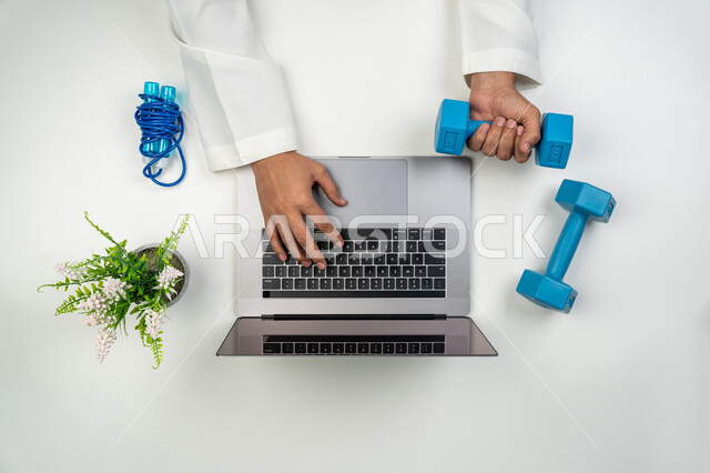 تقديم خدمات الرعاية البدنية أونلاين, إنجاز العمل باستخدام الأجهزة التقنية الحديثة, بورتريه علوي عامودي ليدين مدرب عربي خليجي إماراتي يقوم برفع الأوزان و بالكتابة على جهاز الحاسوب, متابعة البرامج الرياضية عبر الانترنت, خلفية بيضاء