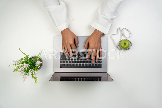 Providing consultations and services remotely, using modern and advanced technologies at work, a vertical portrait of two hands, an Arab-Gulf-Emirati nutritionist writing on a laptop, taking care of physical health, white background
