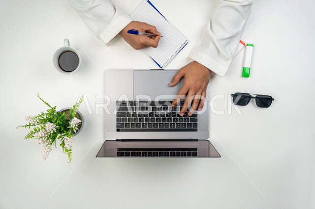 Collecting results and information, taking notes, identifying important points, using modern technical devices, vertical overhead portrait of an Arab, Gulf, and Emirati man using a laptop to search for information, white background.