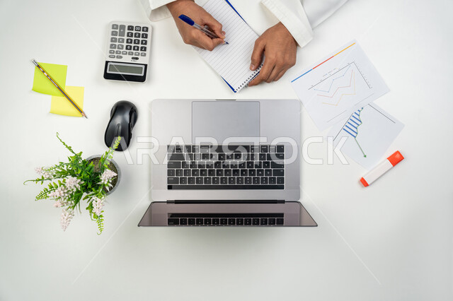 استخدام التكنولوجيا الحديثة في العمل, تسجيل الملاحظات الهامة, مهن و وظائف مكتبية, بورتريه علوي عامودي ليدين رجل عربي خليجي إماراتي يقوم بالكتابة على الدفتر, خلفية بيضاء