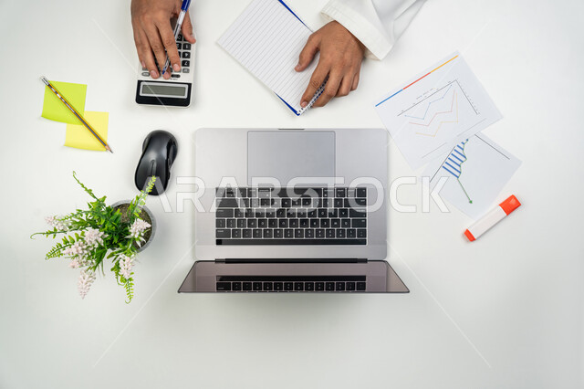 Completing work tasks, using modern technical devices to collect results and solve problems, office professions and jobs, a vertical overhead portrait of the hands of an Arab Gulf-Emirati man using a calculator, white background.
