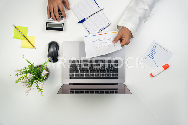 Integrating advanced technology with work, studying and analyzing statistics and graphs, a vertical portrait of the hands of an Arab Gulf Emirati man using a calculator, collecting stock market and stock market data, white background.