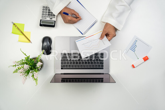 دراسة و تحليل الإحصائيات و الرسوم البيانية, دمج التكنولوجيا المتطورة مع العمل, بورتريه علوي عامودي ليدين رجل عربي خليجي إماراتي يقوم بتسجيل الملاحظات على الدفتر,  جمع بيانات البورصة و سوق الأسهم,, خلفية بيضاء