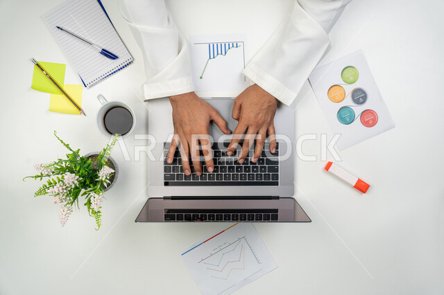 Supervising office work, integrating modern technologies into practical life, a vertical overhead portrait of an Arab Gulf Emirati man studying and analyzing statistics and graphs via a computer, collecting stock market and stock market data, white background