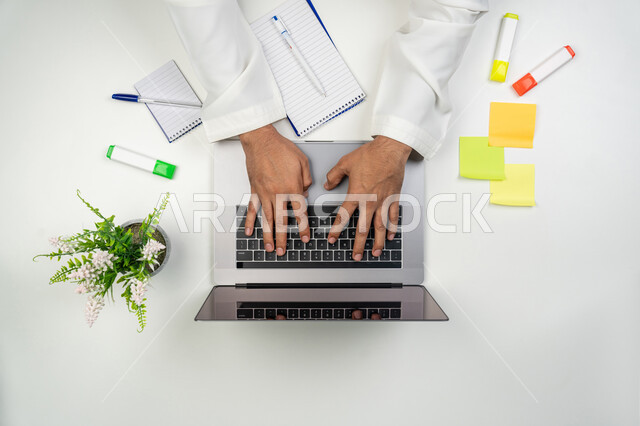 تسجيل الملاحظات المهمة, مهن و وظائف مكتبية, استخدام الأجهزة التقنية الحديثة لإنجاز الأعمال, بورتريه علوي عامودي ليدين رجل عربي خليجي إماراتي يقوم بالنقر على لوحة المفاتيح, بيئة العمل المكتبي المريح, خلفية بيضاء
