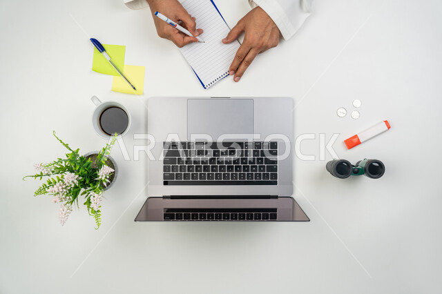 Using advanced technologies in daily life, completing office work, recording important notes, vertical overhead portrait of an Arab Gulf Emirati man writing on a notebook, comfortable office work environment, white background