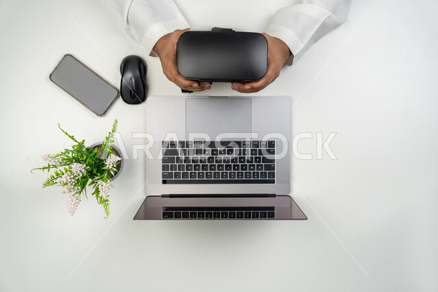 العلوم والتكنولوجيا الحديثة والمتطورة, استخدام نظارات الواقع الافتراضي, بورتريه علوي عامودي ليدين رجل عربي خليجي إماراتي يمسك بيديه نظارة الفي ار, خلفية بيضاء