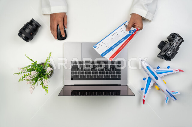 مفهوم السياحة و السفر, استخدام التقنيات الحديثة لإعداد الرحلات الترفيهية في أوقات الفراغ, بورتريه علوي عامودي ليدين رجل عربي خليجي إماراتي يمسك بيده وثيقة حجز, عمليات الحجز الالكتروني عبر جهاز الحاسوب المحمول, خلفية بيضاء