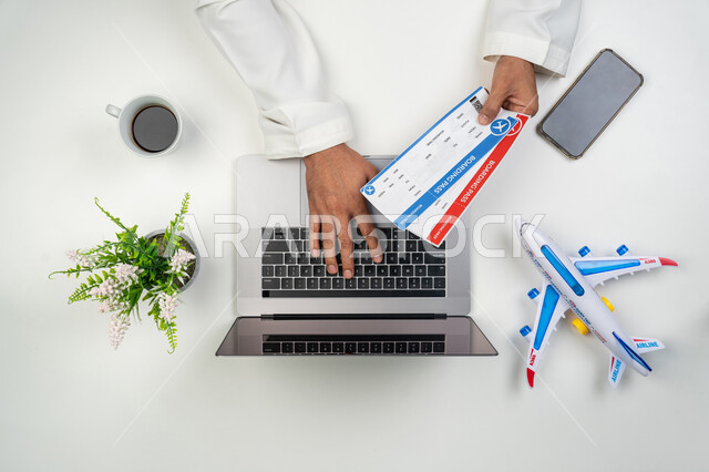 التحضير للسفرات و الرحلات, استخدام التقنيات الحديثة للحجز الالكتروني عن بعد, بورتريه علوي عامودي ليدين رجل عربي خليجي إماراتي يمسك بيده تأشيرتا السفر و يقوم بالنقر على لوحة المفاتيح, خلفية بيضاء