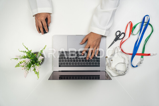 الوصول إلى دورات تعليمية عبر الانترنت, استخدام التقنيات الحديثة بالحياة العملية, ممارسة مهنة الخياطة, بورتريه علوي عامودي لمصمم أزياء عربي خليجي إماراتي  يستخدم جهاز الحاسوب المحمول لإنشاء و تعديل أنماط الخياطة بسرعة و دقة, التواصل مع العملاء و الموردين, خلفية بيضاء