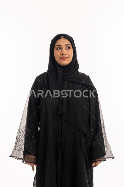 ايماءات السرور والسعادة، الاهتمام بالمظهر الخارجي، مفهوم الانوثة والاناقة، بورتريه لامرأه عربيه خليجيه اماراتيه مبتسمة ترتدي عباءة سوداء تنظر إلى الكاميرا بتعابير الفرح، شابة سعودية انيقة، خلفية بيضاء