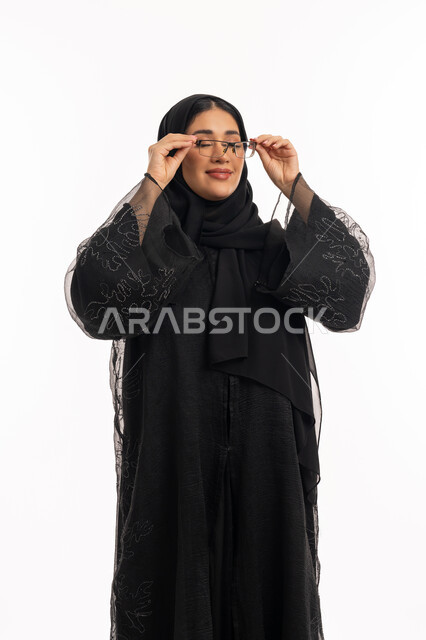تحسين الرؤية ومحاولة تعديل البصر، ارتداء النظارات الخاصة بضعف النظر، الاناقة والاهتمام بالمظهر الخارجي، بورتريه لامرأة عربية خليجية اماراتية محجبة ترتدي عباءة سوداء تمسك بيدها نظارة طبية، شابة سعودية انيقة، خلفية بيضاء