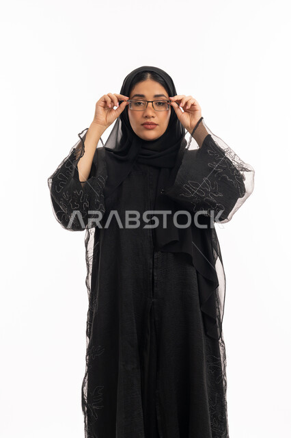 تحسين الرؤية ومحاولة تعديل البصر، ارتداء النظارات الخاصة بضعف النظر، الاناقة والاهتمام بالمظهر الخارجي، بورتريه لامرأة عربية خليجية اماراتية محجبة ترتدي عباءة سوداء تمسك بيدها نظارة طبية، شابة سعودية انيقة، خلفية بيضاء