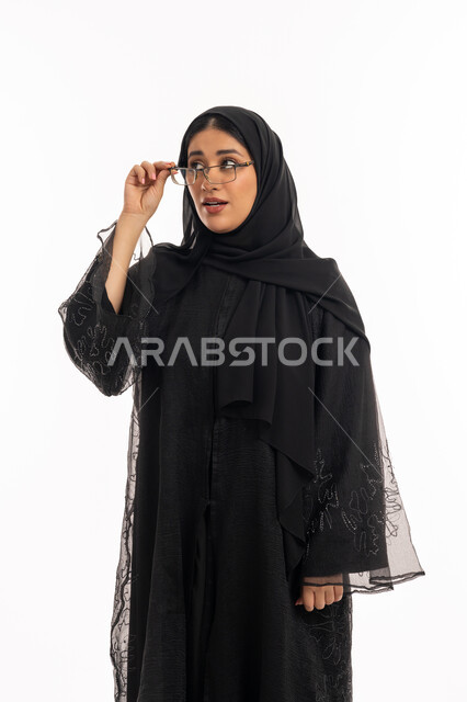 ارتداء النظارات الخاصة بضعف النظر، الاناقة والاهتمام بالمظهر الخارجي، بورتريه لامرأة عربية خليجية اماراتية محجبة ترتدي عباءة سوداء تمسك بيدها نظارة طبية، تحسين الرؤية ومحاولة تعديل البصر، شابة سعودية انيقة، خلفية بيضاء