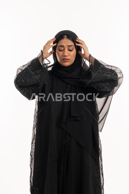 الإحساس بألم الرأس والصداع، الحاجة للهدوء والراحة، المعاناة من آلام الشقيقة، بورتريه لإمرأة عربية خليجية اماراتية محجبة ترتدي عباءة سوداء تضع يديها على رأسها بايماءات التعب والارهاق، شابة سعودية مريضة، خلفية بيضاء