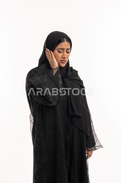 تسوس الأضراس وإلتهاب اللثه، طلب العلاج و المساعده، بورتريه من الجانب لامرأه عربيه خليجيه اماراتية محجبة ترتدي عباءة سوداء تضع يدها على خدها بإيماءات تدل على الشعور بألم الأسنان، الحاجه لزيارة الطبيب، شابة سعودية مريضة، خلفية بيضاء